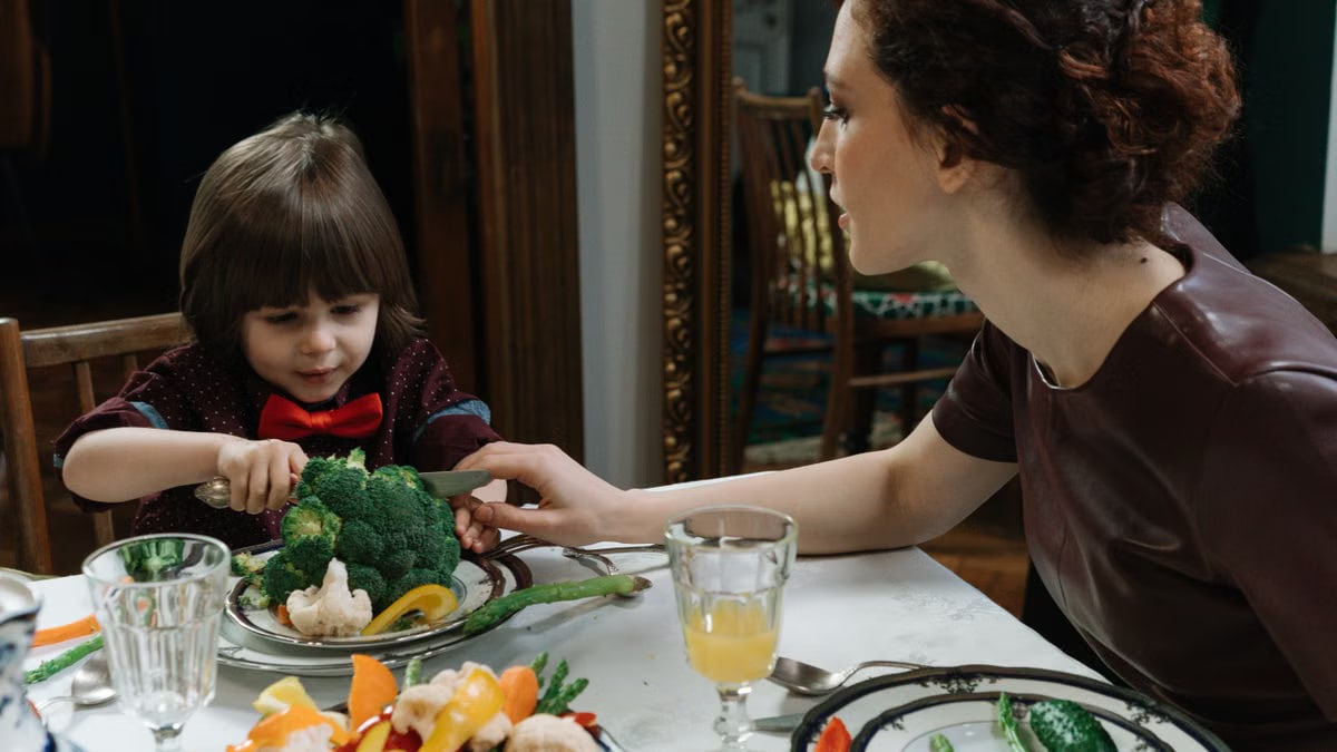 A young boy and a woman sharing a meal with vegetables, promoting healthy eating habits.